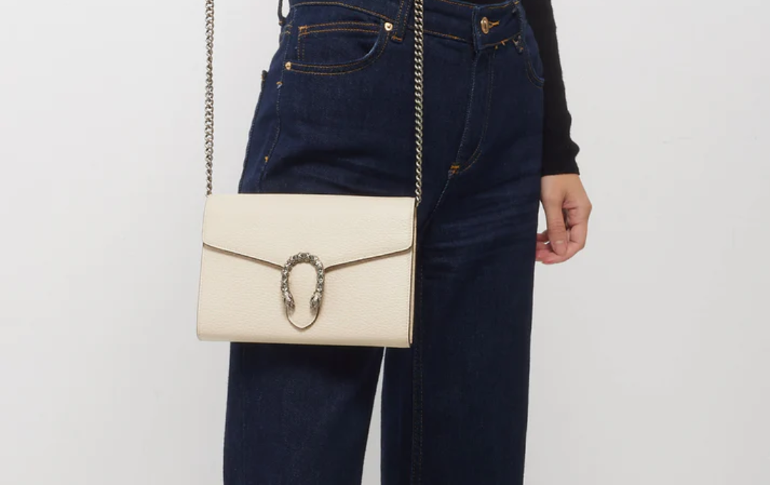 Close-up shot of a white GUCCI WALLET WITH CHAIN bag resting on a marble table.